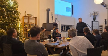 Teilnehmer des Hintergrundgesprächs zum Bauwerksbuch in Wien am 18.11.2025 lauschen aufmerksam einem Vortragenden in einem Besprechungsraum mit vorweihnachtlicher Atmosphäre