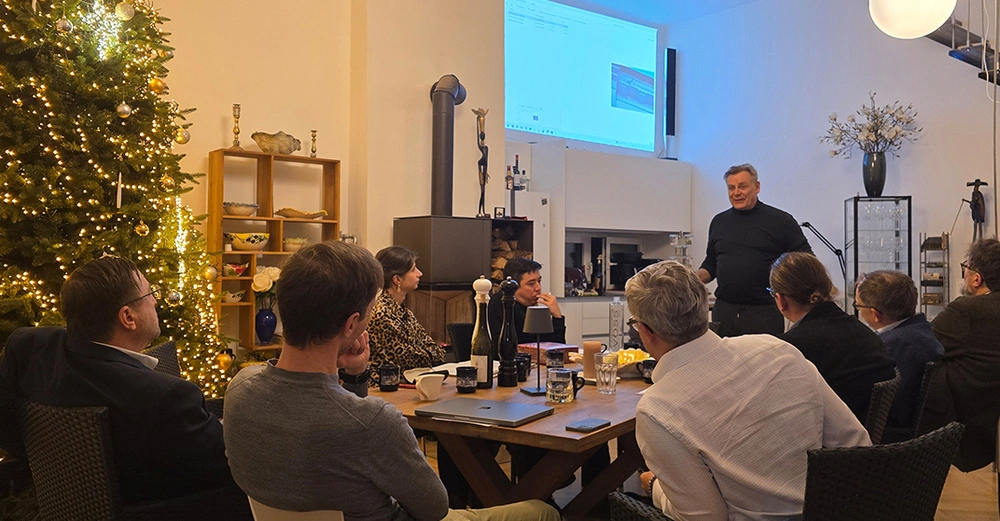 Teilnehmer des Hintergrundgesprächs zum Bauwerksbuch in Wien am 18.11.2025 lauschen aufmerksam einem Vortragenden in einem Besprechungsraum mit vorweihnachtlicher Atmosphäre