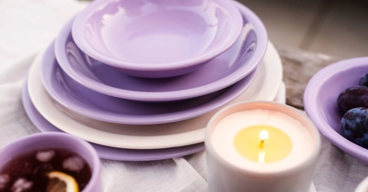 Stapel aus fliederfarbenen und weißen Tellern von Gmundner Keramik, dekoriert mit einer brennenden Kerze und frischen Früchten.
