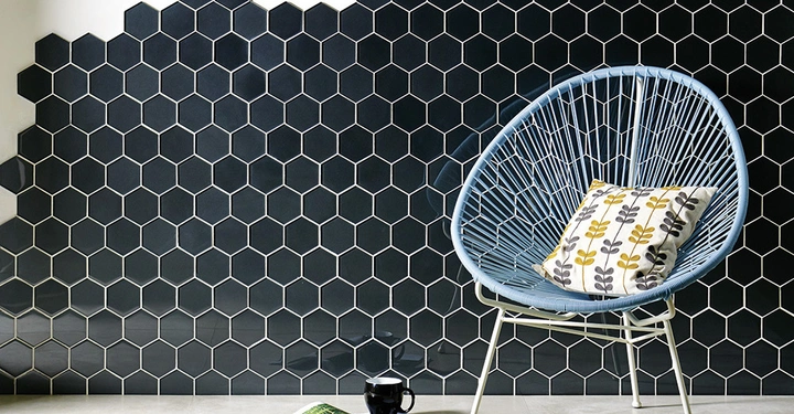 Galerie-Bild 6: Ein blauer Stuhl hält ein gemustertes Kissen und steht vor einer Wand mit schwarzen Sechseckfliesen. Auf dem Boden liegen eine offene Zeitschrift und eine Kaffeetasse.