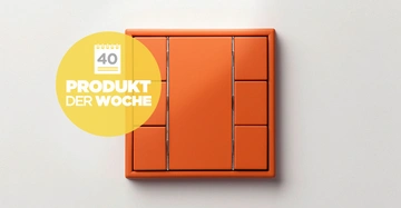Orangener Lichtschalter an einer weißen Wand mit einem gelben Kreis neben dem Schalter Text im Kreis 40 PRODUKT DER WOCHE.