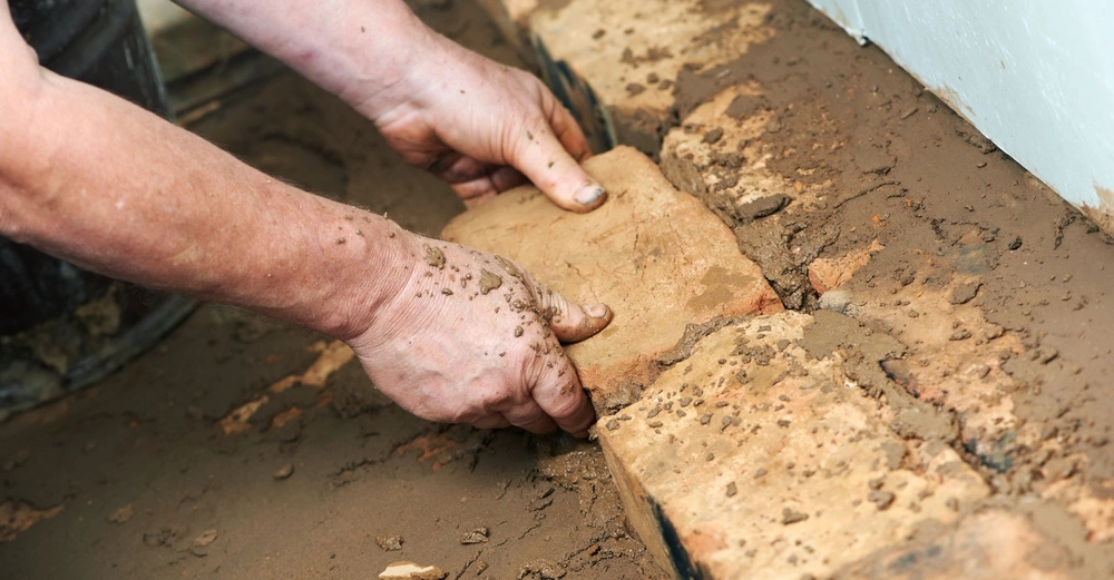 Hände legen einen Ziegelstein in nassen Mörtel während des Bauens einer Ziegelmauer in einem Gebäude.