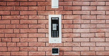 Türsprechanlage mit Kamera und Tastenfeld montiert an roter Backsteinwand den Innenraum beleuchtend Ezviz-Gerät Nr. 38010 darunter Textanzeige Fasttel oben auf Display klingelnder Türknopf abgebildet