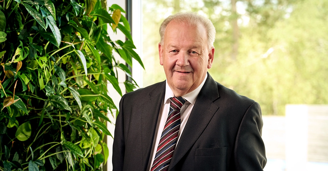 Michael Drexl in blauem Anzug und gestreifter Krawatte steht lächelnd vor Glasfenster und lebender Wand.