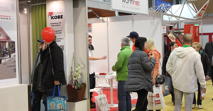Galerie-Bild 24: Menschen unterhalten sich und erkunden Messestände in einer Ausstellungshalle. Text auf dem Stand: "IKOBE Gallenberg 17b 4950 Altheim Innengstadt 3 8052 Hohenems Siedlungsstraße 2 4300 St. Pölten" "wohnnet WO UND WIE WOHNEN".