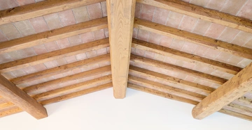 Holzbalken stützen eine Ziegeldecke in einem hohen Raum mit weißen Wänden