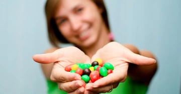 Eine Person hält eine Handvoll bunter Schokolinsen vor sich. Die Person trägt ein grünes Oberteil und der Hintergrund ist unscharf.