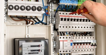 Handwerker prüft Sicherungen in Zählerkasten mit Strommessgerät.