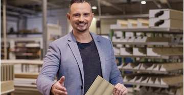 Junger Mann in legerem Businesslook steht in Verkaufsraum und streckt die Hand entgegen.