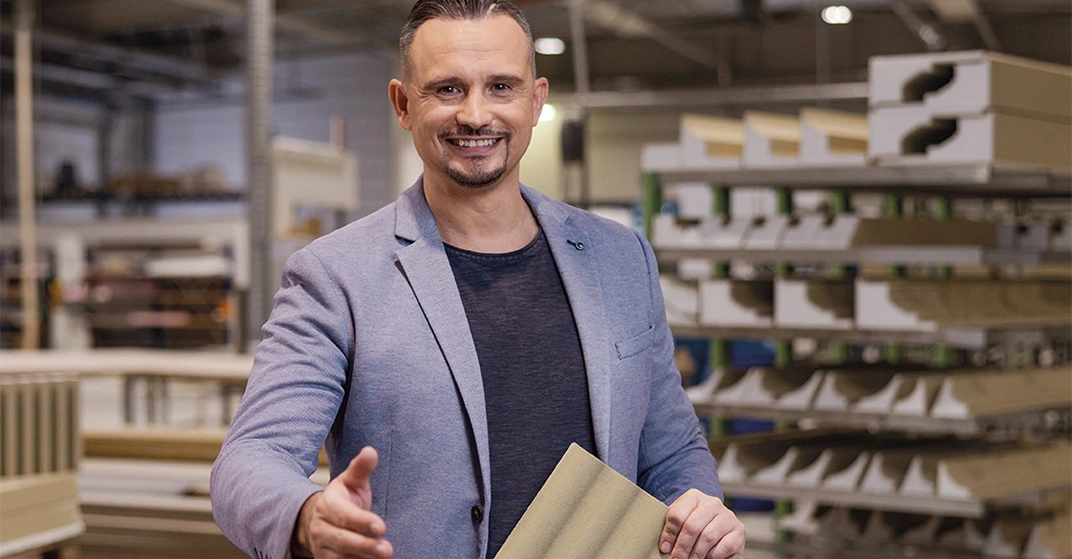 Junger Mann in legerem Businesslook steht in Verkaufsraum und streckt die Hand entgegen.