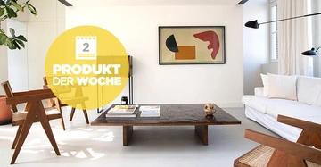 Ein moderner Wohnraum mit Holztisch und Stühlen eine weiße Couch im Hintergrund und eine Kunstwerk an der Wand Text auf gelbem Kreis Produkt der Woche 2.