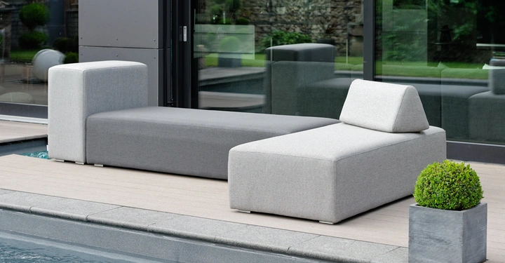 Galerie-Bild 8: Graues Lounge-Sofa steht auf einer Holzterrasse neben einem Pool und ist vor einer großen Panoramafensterfront platziert; daneben steht ein quadratischer Pflanztopf mit grünem Strauch.
