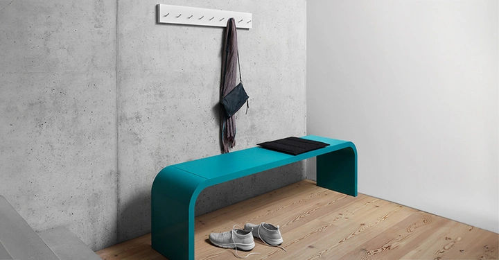 Galerie-Bild 11: Längliche Sitzbank mit abgerundeten Kanten in Türkis von Müller Möbel, auf der Betonwand dahinter eine weiße Hakenleiste, auf der eine schwarze Tasche und ein dunkelbrauner Schal hängt