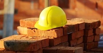 Ein gelber Bauhelm liegt auf einem Stapel roter Ziegelsteine auf einer Baustelle im Freien bei Tageslicht
