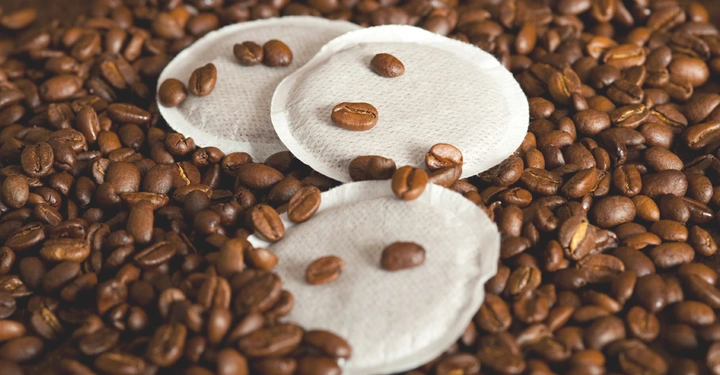 Kaffeepads liegen mit Kaffeebohnen bedeckt auf einem Haufen aus Kaffeebohnen.