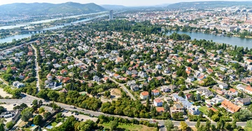 Häuser und Gebäude breiten sich bis zum Horizont aus Ruheviertel umgeben von Grün und Flüssen Hügel und eine entfernte Stadt im Hintergrund.