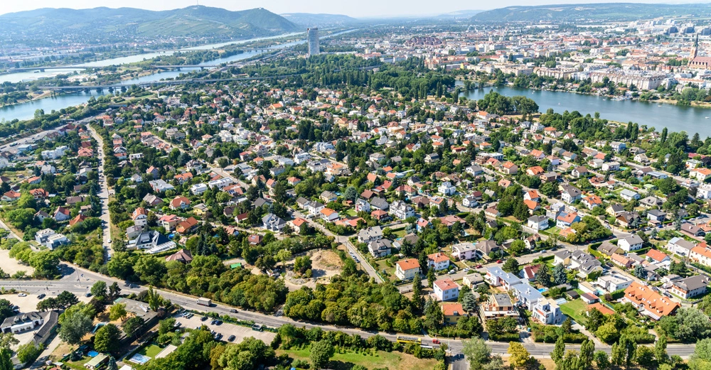 Häuser und Gebäude breiten sich bis zum Horizont aus Ruheviertel umgeben von Grün und Flüssen Hügel und eine entfernte Stadt im Hintergrund.