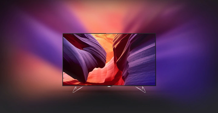 Galerie-Bild 6: Fernseher zeigt bunte Naturaufnahme einer Felsenschlucht im Vordergrund in einem dunklen Raum mit violett-orangefarbener Beleuchtung im Hintergrund.