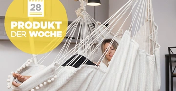 Eine Frau liegt in einer weißen Hängematte und entspannt sich in einem modernen Wohnzimmer mit grauen Möbeln. Text im Bild: 28 PRODUKT DER WOCHE