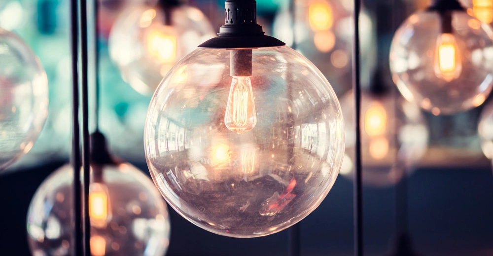 Klarglühbirnen hängen von schwarzen Kabeln beleuchtet eine warme gelbe Glühbirne in der Mitte in einem farbenfrohen unscharfen Hintergrund in einem modernen Raum.