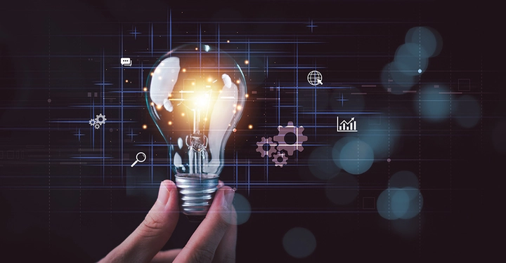 Eine Hand hält eine Glühbirne vor einem dunklen Hintergrund mit Symbolen, die für Ideen und Digitalisierung stehen.