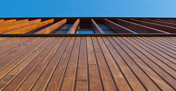 Holzverkleidete Fassade steigt nach oben Kontext strukturiertes Holz mit vertikalen Lamellen vor einem klaren blauen Himmel