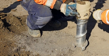 Arbeiter mit Hanschuhen montieren eine neue Bohrspitze zur Bodenbohrung in Erde