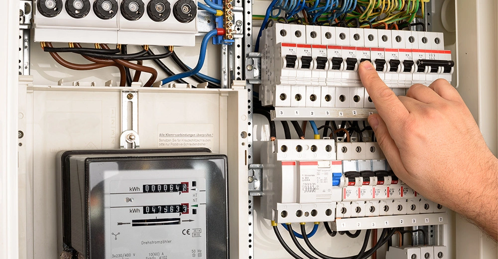 Zählerkasten Check: Mann schaltet herausgefallene Sicherung im Zählerkasten wieder ein. Links im Bild Heizungszähler, rechts Sicherungen.