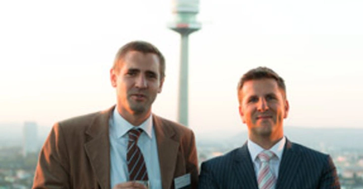 Galerie-Bild 22: Zwei Männer stehen nebeneinander auf einem Balkon Der erste Mann hält ein Getränk Der zweite Mann hat die Arme verschränkt Im Hintergrund ist ein großer Fernmeldeturm zu sehen