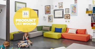 Zwei Kinder spielen mit Spielzeug in einem Wohnzimmer mit bunten Sofas vor einer Wand mit Bilderrahmen und Regalen Text im Bild 35 PRODUKT DER WOCHE