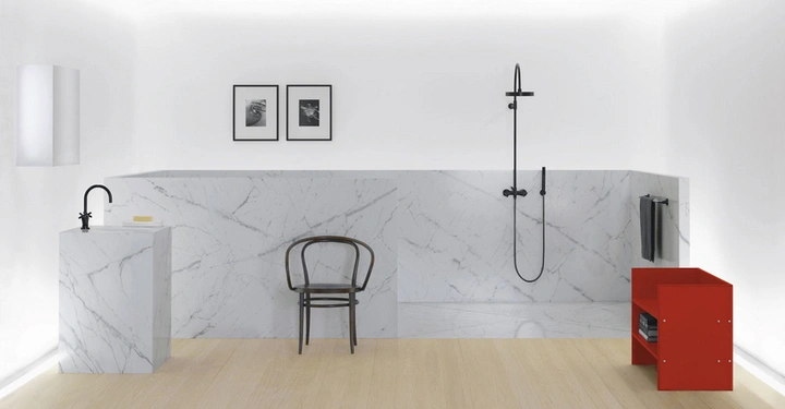 Galerie-Bild 2: Ein schwarzer Stuhl steht auf einem hellen Holzboden vor einer weiß-marmorierten Wand mit Duschkopf in einem minimalistisch eingerichteten Badezimmer neben einem roten Regal.