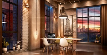 Ein Tisch mit vier Stühlen und einem offenen Laptop in einem modern eingerichteten Loft mit großen Fenstern bei Sonnenuntergang, einer industriellen Backsteinwand und dekorativen Pflanzen.