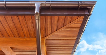 Braunes Dach mit Holzverkleidung und Regenrinne Blauer Himmel mit einigen Wolken im Hintergrund