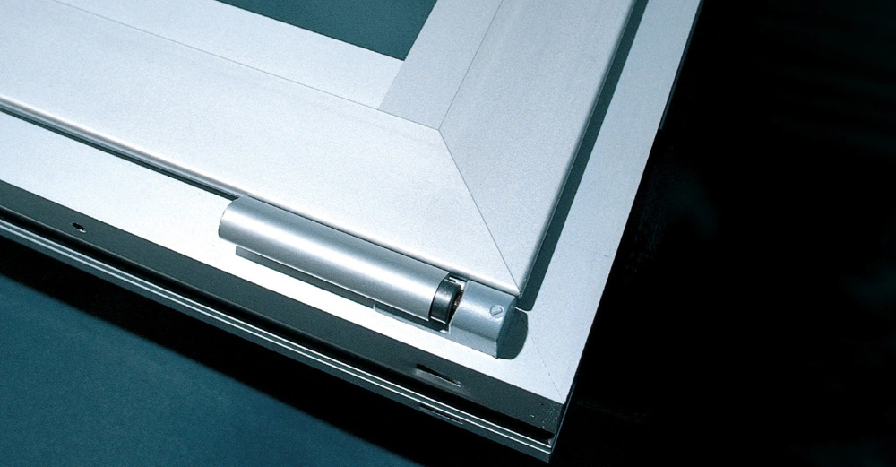 Ein silbernes Scharnier verbindet einen Fensterrahmen in Nahaufnahme in einer dunklen Umgebung. Es wird von oben betrachtet, zeigt saubere und klare Linien sowie eine moderne Ausführung.