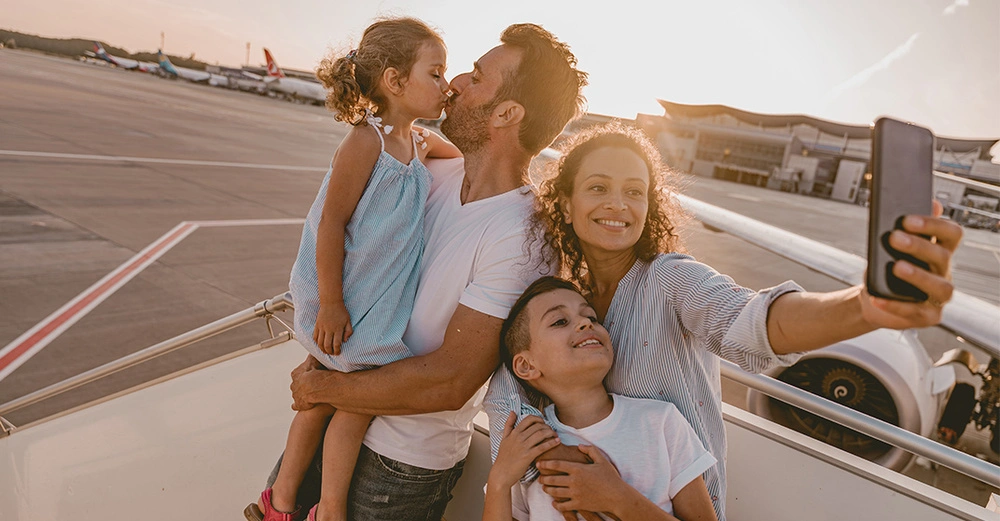 Glückliche Familie macht Selfie am Flughafen vor dem Abflug. Warnung vor Urlaubs-Posts auf Social Media, da sie Einbrecher anlocken können.