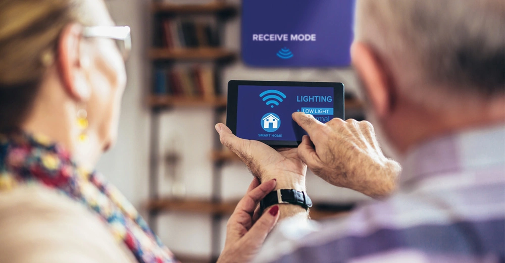 Altes Ehepaar von hinten fotografiert tippt auf Tablet, um das Smart Home einzurichten. Frau trägt Brille und Haarknoten, Mann hat Halbglatze