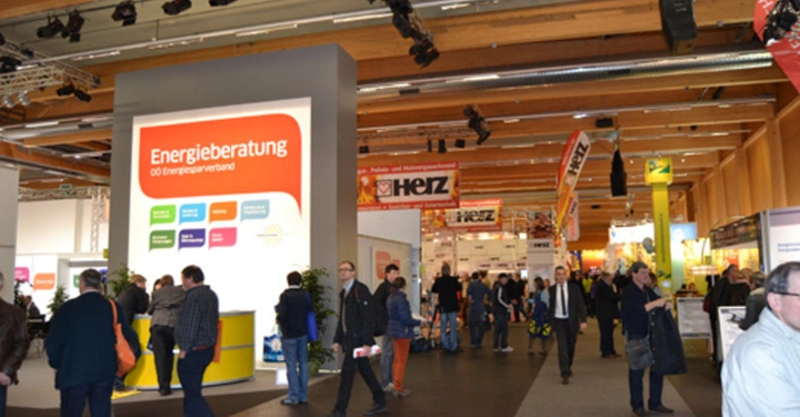 Galerie-Bild 32: Großer Ausstellungsraum mit vielen Menschen die zwischen Ständen mit farbenfrohen Schildern gehen Ein Schild zeigt den Text Energieberatung OO Energiesparverband und verschiedene Dienstleistungen