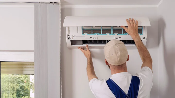 Handwerker in blauem Overall installiert das Innengerät einer Split-Klimaanlage in einer modernen Wohnung.