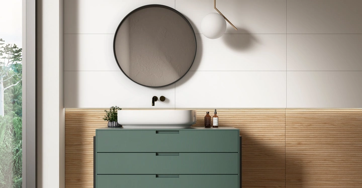 Grüner Waschtisch mit weißem Waschbecken und runder Spiegel an der Wand In einem modernen Badezimmer mit weißen Fliesen und Holzverkleidung Links ist ein Fenster mit Blick auf grüne Vegetation