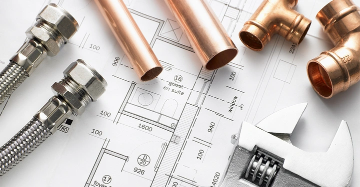 Metallrohre und Sanitärzubehör liegen auf technischen Zeichnungen in einem baulichen Planungsumfeld