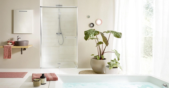 Waschbecken auf Holzregal mit roten Handtüchern und Zubehör vor beigefarbener Wand daneben eine Dusche mit Glastüren sowie Topfpflanzen und dekorativen Gegenständen neben einer Badewanne in einem hellen Badezimmer.