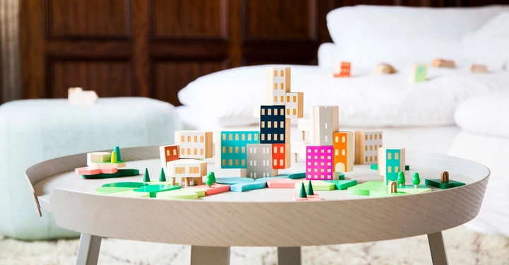 Farbenfrohe Holzgebäude stehen auf einem runden Tisch in einem Wohnzimmer mit Teppich und Holzwänden Im Hintergrund sind weiße Möbelstücke zu sehen