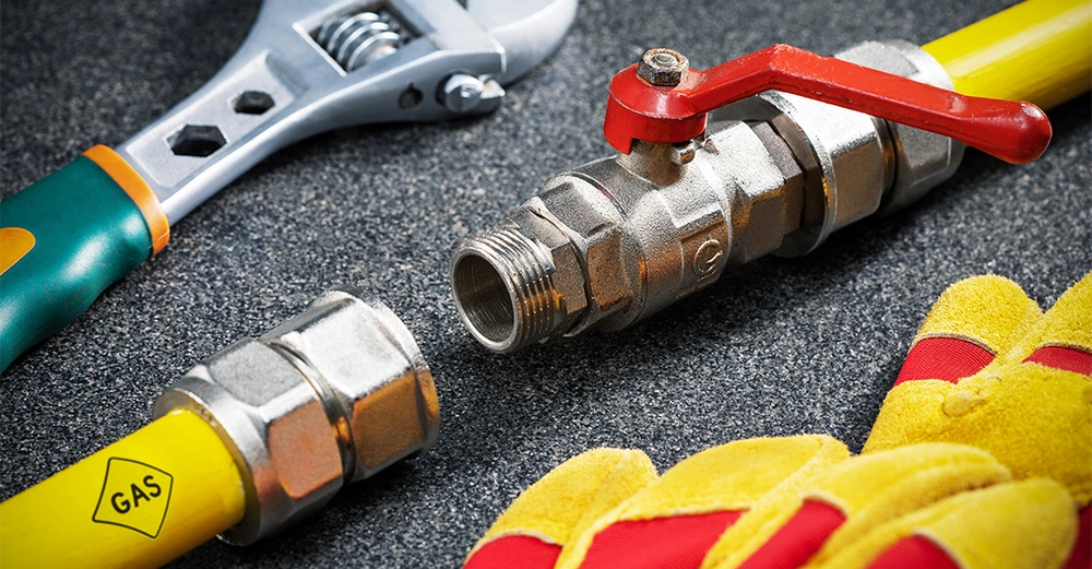 Eine gelbe Gasleitung liegt neben einem Arbeitshandschuh und einem Schraubenzieher auf einem dunklen Untergrund. 