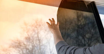 Hand zieht eine Fensterfolie auf einem Fenster auf an einem bewölkten Tag Bäume und Himmel sind draußen unscharf sichtbar