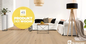 Ein weißes Sofa mit Kissen steht in einem modernen Wohnzimmer mit Holzfußboden. Ein Couchtisch mit Obst, eine Stehlampe und Pflanzen umgeben das Sofa. Text: 45 Produkt der Woche Scheucher.