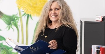 Andrea Höllbacher von Glorit steht in Büro und hält Bauhandbuch in der Hand