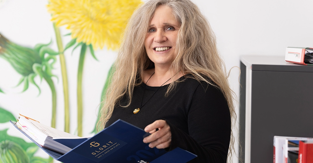 Andrea Höllbacher von Glorit steht in Büro und hält Bauhandbuch in der Hand