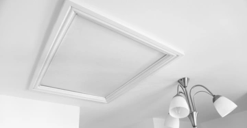 Eine weiße Deckenluke ist geschlossen, daneben hängt eine dreiflammige Deckenleuchte mit weißen Lampenschirmen im modernen Wohnraum.