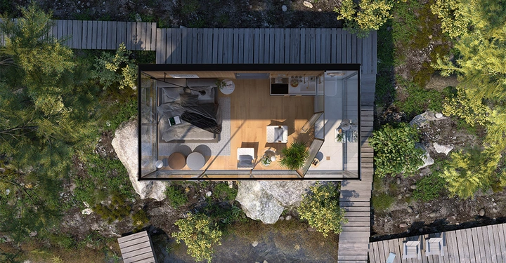 Kleines verglastes Häuschen mit Bett Esstisch und Kitchenette in einer bewaldeten Felslandschaft von Holzstegen umgeben