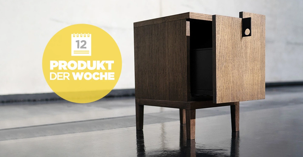 Holzschrank steht leicht geöffnet auf einem glänzenden Boden in einem modernen, minimalistischen Raum. Ein gelber Kreis enthält einen Kalender mit der Zahl 12 und den Text PRODUKT DER WOCHE.